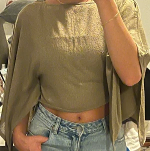 Stickad topp med capearm / breda armar / fladdermusarm H&M stl XS - Khakigrön - Superfin slutsåld stickad topp från H&M:s Divided-kollektion i en snygg khakigrön nyans. Toppen är i en croppad modell med långa, fladdrande capeärmar som ger en dramatisk och stilsäker silhuett. Perfekt till höga jeans eller kjol!  Storlek XS, passar även mig som har S.   Mycket gott skick