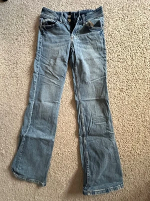 Ljusblå bootcut jeans  - Ljusblå bootcut jeans med dubbla knappar i midjan och bakfickor med lock och knapp. Köpte de secondhand, men har använt de 2 gånger.