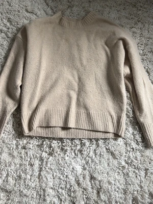 Beige stickad tröja från Zara - Mysig beige stickad tröja från Zara med rund halsringning och ribbade muddar vid ärmslut och nederkant. Perfekt för lager på lager och enkel att matcha med olika outfits. Tillverkad i mjukt material .