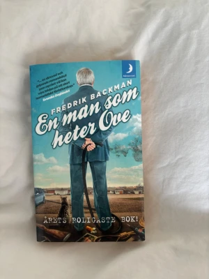 En man som heter Ove pocket - En man som heter Ove av Fredrik Backman i pocketformat. Omslaget är blått med en illustration av en man i kostym som står med händerna bakom ryggen. Boken är tryckt på papper och har text på svenska. Perfekt för dig som gillar humoristisk och varm skönlitteratur.