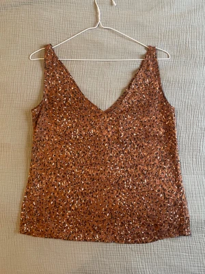 Brun leopardmönstrad linnetopp - Snygg brun linnetopp med leopardmönster och v-ringad hals. Toppen är ärmlös och har en avslappnad passform, perfekt för att lyfta vilken outfit som helst. Materialet känns lätt och luftigt, vilket gör den skön att bära under varma dagar.