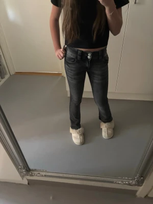 Svarta bootcut jeans med dubbla knappar - Säljer ett par svarta bootcut jeans med snygg tvätt och dubbla knappar i midjan. Jeansen har fickor både fram och bak med detaljerade sömmar och vita knappar bak. Perfekta för dig som gillar en lite retro vibe och vill ha ett par jeans som sticker ut.