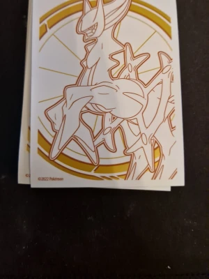 Pokémon sleeves 30 st Arceus & 50 st Mew - Säljer två högar Pokémon sleeves, ett med Arceus i guld och vitt och ett med Mew i rosa på lila bakgrund med blå detaljer. Officiella Pokémon-motiv från 2021 och 2022.