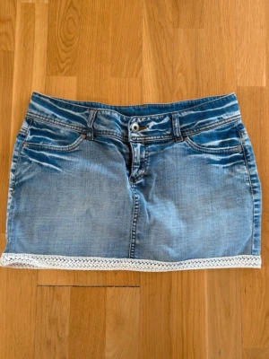 Blå jeanskjol med spets! - Säljer en blå kort jeanskjol med vit spetsdetalj längst ner och på bakfickorna. Kjolen har klassiska jeansfickor fram och bak. Superskön och lowrise men lagom kort ⭐️SKRIV FÄRNA VID FRÅGOR