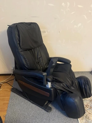 Svart elektrisk massagefåtölj - Elektrisk massagefåtölj i svart konstläder med bred sits, högt ryggstöd och fotstöd. Utrustad med armstöd, inbyggd fjärrkontroll och trädetaljer på sidorna. Perfekt för att slappna av och få massage hemma.
