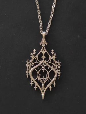 Silvrigt halsband med gotiskt hänge - Vackert halsband i silverfärgad metall med ett detaljerat, gotiskt inspirerat hänge. Hänget har spetsiga former och intrikata mönster. Kedjan är tunn och matchar hängets färg. Perfekt för dig som gillar alternativ stil och snygga detaljer.
