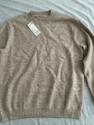 Beige stickad tröja med rund hals - Snygg beige stickad tröja med rund hals och ribbade muddar vid ärmslut och nederkant. Tröjan har en enkel och stilren design som passar perfekt till lager-på-lager. Tillverkad i mjukt material för extra komfort.