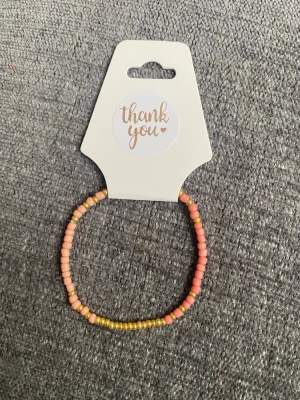 Pärlarmband i rosa och gult - Sött armband med små pärlor i rosa och gult. Armbandet har en enkel och stilren design med elastisk tråd som gör det lätt att ta på och av. Perfekt för att addera lite färg till din outfit.