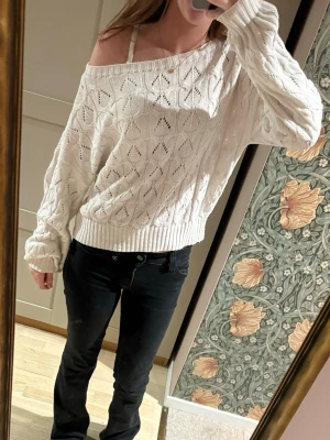 Vit off shoulder stickad tröja - Säljer en vit stickad tröja med off shoulder-modell och löst sittande passform. Tröjan har ett fint hålmönster, bred ribbad mudd i nederkant och vid ärmslut. Perfekt för dig som gillar en avslappnad och trendig stil.