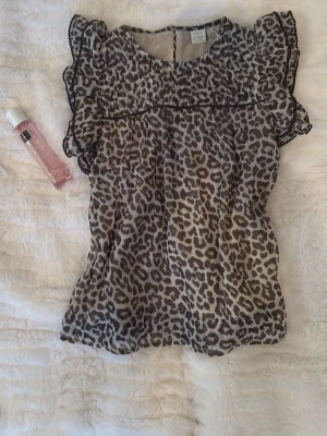 Leopardmönstrad blus från Lindex - Säljer en luftig leopardmönstrad blus från Lindex med volangdetaljer vid axlarna och korta ärmar. Blusen har rund halsringning och är tillverkad i ett tunt, skönt material som passar perfekt till din stil.🫰🏻💓( kan pruta ner priser)