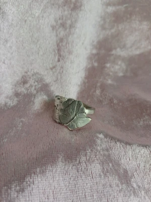 Handgjord ring nysilver 18/58 - Handgjord ring skapat av en sked gjord i nysilver. Ringen består av ett lövmönster,blomma samt en fjäril. Storlek 18/58 beroende på hur man mäter 