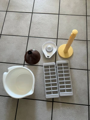 Köksprylar blandat set - Säljer ett blandat set med köksprylar: vit plastbunke med handtag, två isbitsformar i plast, brun tratt, vit citruspress och gul hushållspappershållare. Perfekt för dig som vill komplettera köket med praktiska tillbehör.