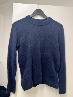 Mörkblå stickad tröja från H&M - Mysig mörkblå stickad tröja från H&M i regular fit. Tröjan har rund halsringning och ribbstickade muddar vid ärmslut och nederkant. Perfekt för kyliga dagar och enkel att matcha med olika outfits.