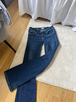 Blå low bootcut jeans från Gina Tricot - Snygga blå bootcut jeans från Gina Tricot med klassisk femficksdesign och kontrastsömmar. De är sydda till lågmidjade jeans och är därför lite tightare i låren. Jeansen har en lätt utsvängd passform och är tillverkade i mjukt denimtyg. Perfekta för en trendig och avslappnad look.
