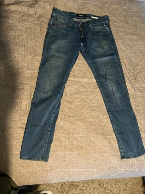 Blå slim fit jeans från Replay - Snygga blå slim fit jeans från Replay med klassisk femficksdesign och dragkedjegylf. Jeansen har diskreta slitningar och kontrastsömmar som ger en cool look. Tillverkade i mjukt denimtyg som sitter skönt hela dagen.