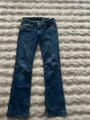 Blå bootcut jeans med slitningar - Snygga blå bootcut jeans med lätt slitna detaljer och klassisk femficksdesign. Jeansen har låg midja och stängs med knapp och dragkedja. Perfekta för en avslappnad och trendig look.