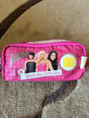 Rosa High School Musical necessär - Säljer en rosa necessär med motiv från High School Musical och texten 'Graduation Celebration'. Väskan har flera fack men smutsiga ifrån pennorna. Perfekt nu för skolstarten.