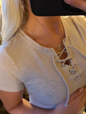 Beige ribbad topp med snörning - beige ribbad topp med korta ärmar och snygg snörning framtill. Croppad modell som sitter tight och har en v-ringad öppning