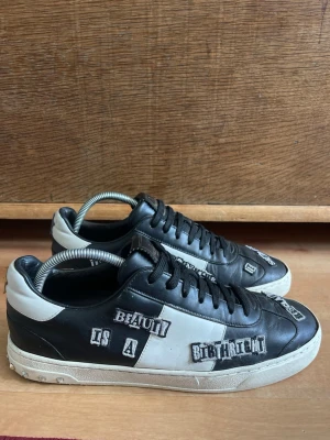 Svarta Valentino Flycrew  - Säljer ett par svarta och vita sneakers från Valentino med coola textpatches och kontrastfärgade detaljer. Skorna har klassisk låg profil, svarta skosnören och vit sula med nitar baktill. Tillverkade i läder för en lyxig känsla.