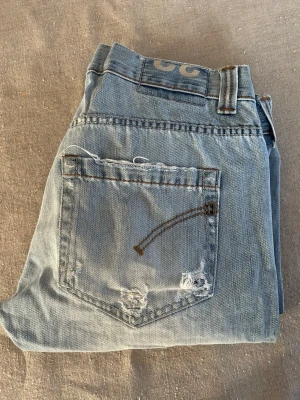 Dondup jeans - Säljer ett par ljusblå jeans med raka ben och slitna detaljer på fickor och ben. Jeansen har klassisk femficksmodell och är gjorda i denim. Perfekta för en avslappnad och trendig look. Skriv gärna om ni har några frågor 