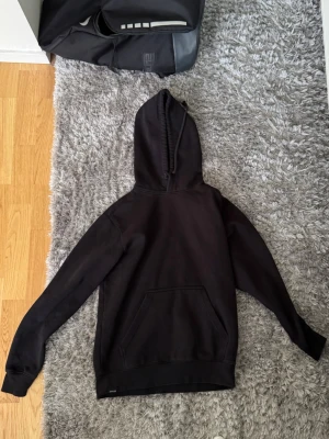 Svart hoodie  - En klassisk svart hoodie med huva och stor magficka framtill. Hoodien har långa ärmar och ribbade muddar vid ärmslut och nederkant. Perfekt för en avslappnad och stilren look. Materialet ser ut att vara mjukt och bekvämt,  bomullsblandning. Xs men passar som S