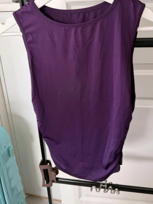 Lila ärmlös tröja i stretchtyg - Säljer en enkel och stilren lila tröja. Tröjan har rund halsringning och är gjord i ett mjukt, stretchigt material som sitter skönt mot kroppen. Perfekt att matcha med jeans eller kjol för en clean look.