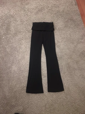 Svarta yogapants med resår vid midjan - Säljer en svart bandeau jumpsuit med hög midja och vida ben. Materialet är mjukt och stretchigt, vilket gör den riktigt bekväm. Perfekt för dig som gillar en enkel men snygg look. Passar till sneakers eller klackar beroende på stil.