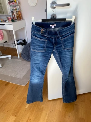 Mörkblå bootcut jeans med fickor - Säljer ett par mörkblå bootcut jeans med stora fram- och bakfickor. Jeansen har markerade sömmar och låg midja. Perfekta för dig som gillar en avslappnad men ändå trendig look. Materialet är klassisk denim i bomull.