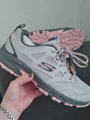 Helt nya vattentäta Skechers sneakers - Snygga sneakers från Skechers i ljusblått med ljusrosa detaljer och mönstrad sula. Skorna har meshpaneler för ventilation, rosa och blå snören samt extra mjuk memory foam-innersula för skön komfort. Perfekta för dig som gillar sportig stil och vill ha bekväma skor. Vattentäta. Helt nya och oanvända!