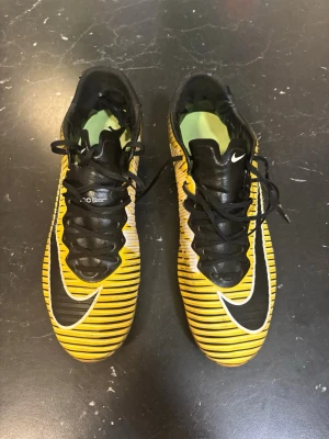 Nike mercurial Vapor 11 - Säljer ett par Nike fotbollsskor med snyggt randigt mönster i gult, svart och vitt. Skorna har snörning, låg profil och tålig syntetöverdel. Perfekta för dig som vill sticka ut på planen med stilrena dobbar och sportig design.
