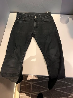 Svarta slim fit jeans - Säljer ett par svarta slim fit jeans med klassisk femficksmodell och knappgylf. Jeansen har en lätt tvättad look och är tillverkade i bomull med lite stretch för skön passform. Perfekta till sneakers eller boots.