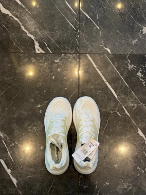 Vita Adidas Ultraboost  - Snygga vita Adidas Ultraboost sneakers med klassiska tre ränder i ljusgul ton på sidan. Ovandelen är i meshmaterial för bra andningsförmåga och sulan är tjock och bekväm. Perfekta för dig som vill ha stilrena och sportiga skor till vardagslooken.
