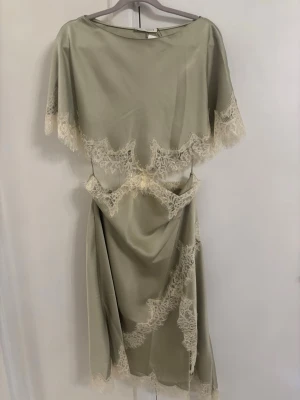 Viral Mintgrön Zara klänning - Elegant ljusgrön långklänning med vackra spetsdetaljer i vitt längs kanterna. Klänningen har en unik omlott-look i midjan och är tillverkad i ett glansigt material som ger en lyxig känsla. Perfekt för speciella tillfällen och sommarens fester.