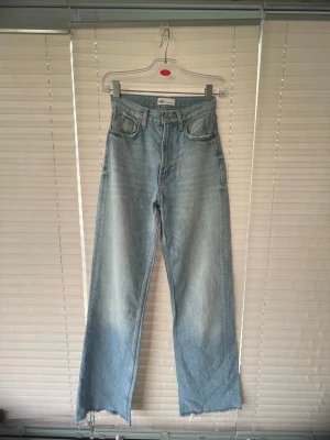 Ljusblå wide jeans från ZARA - Säljer ett par ljusblå jeans från ZARA med hög midja och raka ben. Jeansen har klassisk femficksdesign och råa, avklippta benslut för en trendig look. Perfekta för dig som gillar en avslappnad och modern stil.
