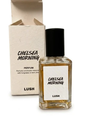 Lush Chelsea Morning parfym - Chelsea Morning från Lush är en parfym i en stilren, rektangulär glasflaska med svart kork. Doften kommer i en vit kartong med svart text. Flaskan har en transparent design som visar den gyllene vätskan inuti.