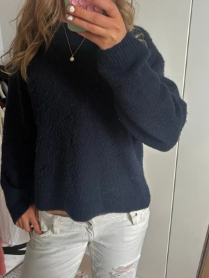 Mörkblå stickad tröja - Mysig mörkblå stickad tröja med avslappnad passform och rund halsringning. Tröjan har långa ärmar och ribbade muddar vid ärmslut och nederkant. Perfekt för kyligare dagar och enkel att matcha med olika outfits.
