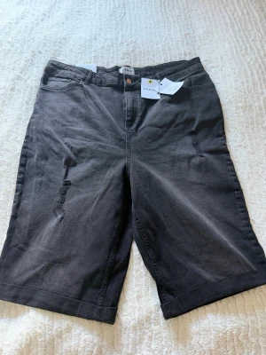Svarta denimshorts  - Säljer ett par svarta denimshorts med klassisk femficksdesign och råa slitningar framtill. Shortsen har knapp och dragkedja samt uppvikta benslut. Perfekta för en avslappnad stil i sommar. Aldrig använda 