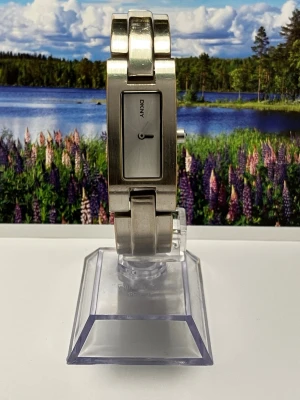 Snygg silverfärgad klocka från DKNY - Stilren klocka från DKNY i silverfärgat metallarmband och rektangulär urtavla. Urtavlan är minimalistisk med diskreta visare och DKNY-logga. Baksidan av armbandet har viss slitage efter användning men påverkar ej varken klockans funktion eller utseende.Perfekt accessoar för dig som gillar en modern och clean look. Nytt batteri, säljes i befintligt skick enligt bilderna!