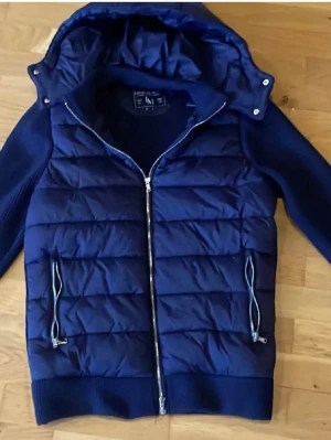  Leon marcel Marinblå cardiganjacka med huva - Snygg marinblå cardiganjacka med vadderad framsida och stickade ärmar samt rygg. Jackan har avtagbar huva, två dragkedjeförsedda fickor och ribbade muddar. Perfekt för lager-på-lager och chill höststil.