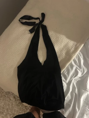 Svart halterneck baddräkt - Stilren svart linnetopp med halterneck och knytband i nacken. Toppen har djup urringning framtill och är ärmlös, vilket ger en trendig och enkel look. Perfekt att matcha med jeans eller kjol för en snygg outfit. Jag har klippt och sytt om en ur ringning till en V ringning och så har jag sytt på band så man kan knyta den i nacken. 💓