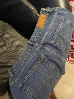 Blåa raka jeans med rå kant - Säljer ett par klassiska blå jeans med raka ben och rå, fransig kant nedtill. Jeansen har hög midja, fem fickor och en snygg vintage-look. Perfekta till sneakers eller boots för en avslappnad stil.