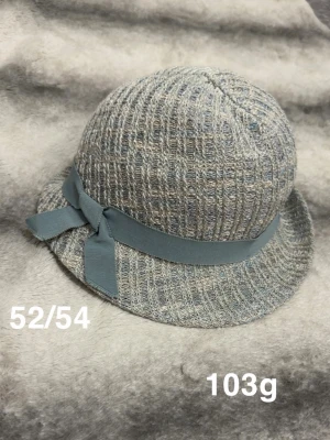  hatt med rosett - Snygg hatt i stickad look med diskret rutmönster och en bred, blå rosett runt kullen. Hatten har en mjuk, rundad form och kort brätte. Perfekt accessoar för dig som vill ha en unik och trendig stil.🌸 Fint använt skick. Storlek 52/54