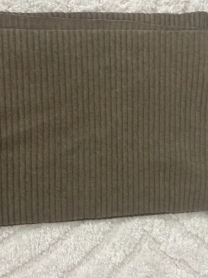 Ribbad halsduk från Design House - Säljer en ribbad halsduk i mjuk beige ull från Design Stockholm House. Halsduken har en stilren och enkel design med tydliga ribbor som ger en modern känsla. Perfekt accessoar för att lyfta din outfit under kyliga dagar.