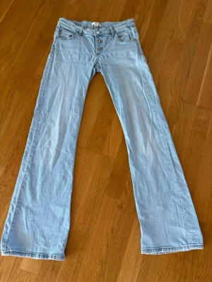Ljusblå bootcut jeans  - Säljer ett par ljusblå bootcut jeans med medel låg midja och knappgylf. Jeansen har klassiska  bakfickor och är tillverkade i mjukt denimtyg. Dem är bara använda två gånger därav är de lite skrynkliga på bilderna.