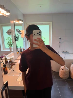 Mörkröd stickad tröja - En enkel och stilren mörkröd stickad tröja med korta ärmar och rund hals. Tröjan har en avslappnad passform och är perfekt för lager på lager. Passar dig som gillar en clean och klassisk look.
