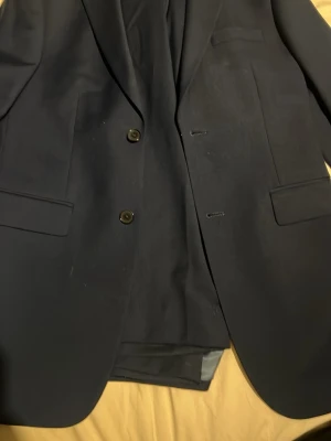 Mörkblå kavaj från Dressmann Slim Fit - Snygg mörkblå kavaj från Dressmann i slim fit-modell. Klassisk tvåknäppt design med två fickor med lock och bröstficka. Fodrad insida och stilren passform. Min gamla student kostym set, använd 1 gång, köpet innehåller båda två delar, ny pris 1899k kr