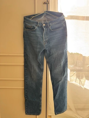 Blå jeans från J.Lindeberg - Klassiska blå jeans från J.Lindeberg med rak passform och fem fickor. Jeansen har en snygg mellanblå tvätt och detaljerade sömmar. Perfekta för en stilren och avslappnad look.