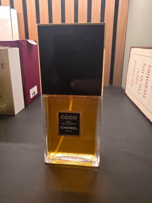 Chanel Coco Eau de Toilette 100ml - Chanel Coco Eau de Toilette i en elegant, rektangulär glasflaska med svart och guld lock. Parfymen har en varm bärnstensfärgad ton och klassisk etikett framtill. Perfekt för dig som gillar lyxiga och tidlösa dofter.