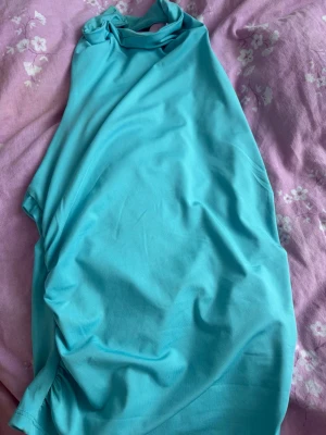 Turkos ärmlös halterneck topp - Säljer en turkos halterneck topp med ärmlös design och öppen rygg. Toppen har en slät yta och är gjord i ett mjukt, stretchigt material som känns skönt mot huden. Perfekt för dig som vill ha en enkel men snygg topp till sommaren.