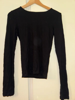 Svart långärmad topp Gina Tricot - En enkel och stilren svart långärmad topp från Gina Tricot. Toppen har en rund halsringning och är tillverkad i ett mjukt och stretchigt material som sitter snyggt på kroppen. Perfekt att matcha med jeans eller kjol för en clean look.